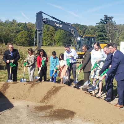 A row of people stand behind a dirt mound while tossing shovelfuls of dirt in front of them.