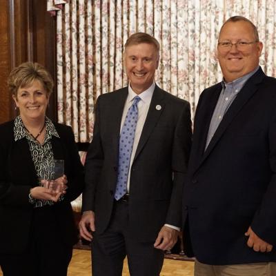 GBS CEO Michele Benson holds a glass plaque while standing next to CSS CEO Bob Stokes and GBS CFO JP Schippert.