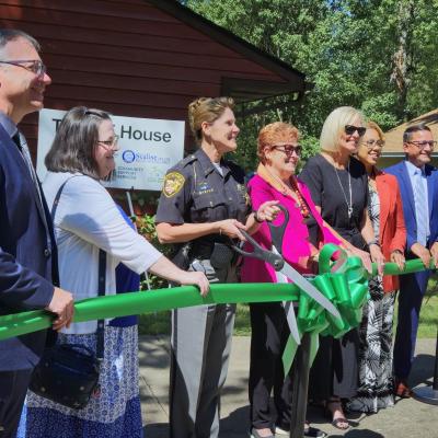 Partners from the THRIVE House prepare to cut a long green ribbon in front of the home.