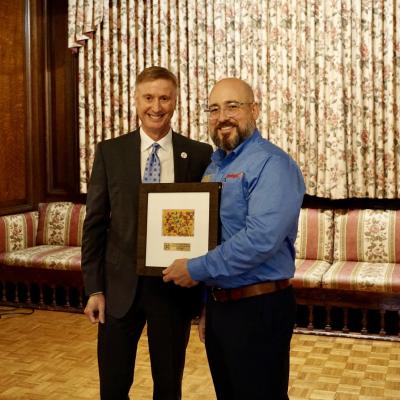 CSS CEO Bob Stokes stands with Jon Novak, who is holding a framed piece of art.